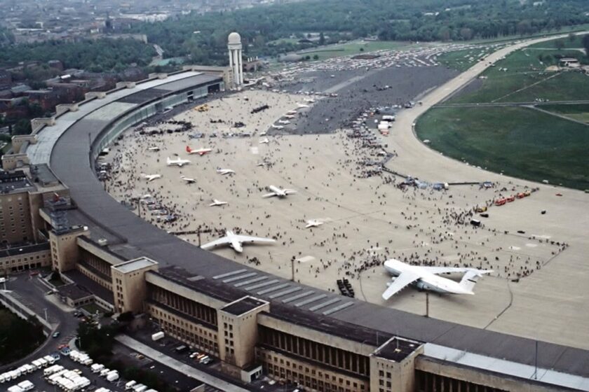 Luftaufnahme des Flughafens Berlin-Tempelhof mit Terminalbogen, Tower, abgestellten Flugzeugen und Menschenmassen auf dem Vorfeld.