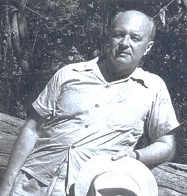 Älterer Mann sitzt im Freien auf einer Holzbank und hält einen hellen Hut; historische Schwarz-Weiß-Aufnahme vor Bäumen.