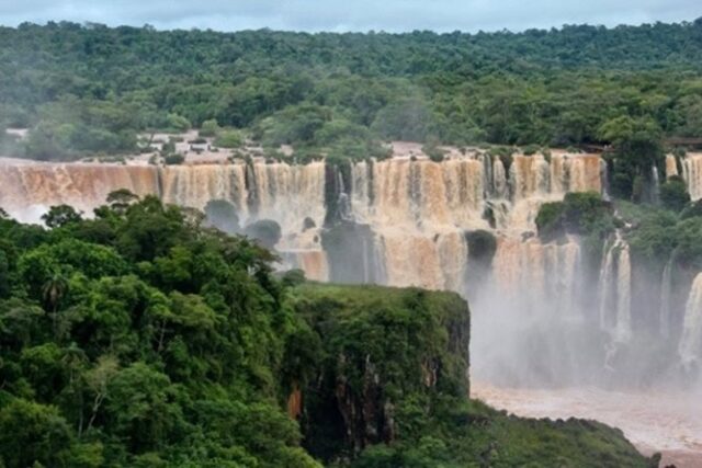 Breite Wasserfälle stürzen in mehreren Kaskaden durch dichten grünen Regenwald, aufsteigender Sprühnebel erfüllt die Schlucht.