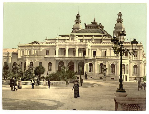 Historische Ansicht eines prunkvollen Gebäudes am Platz mit Laterne, Palmen und Spaziergängern, vermutlich Opernhaus in Monte-Carlo