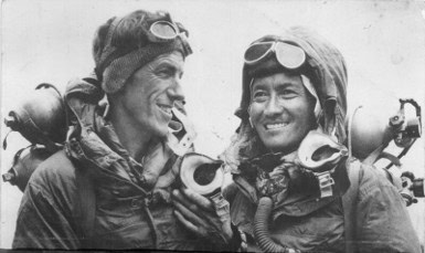 Zwei Piloten in Fliegerjacken und Schutzbrillen, lachend vor dem Flugzeug.